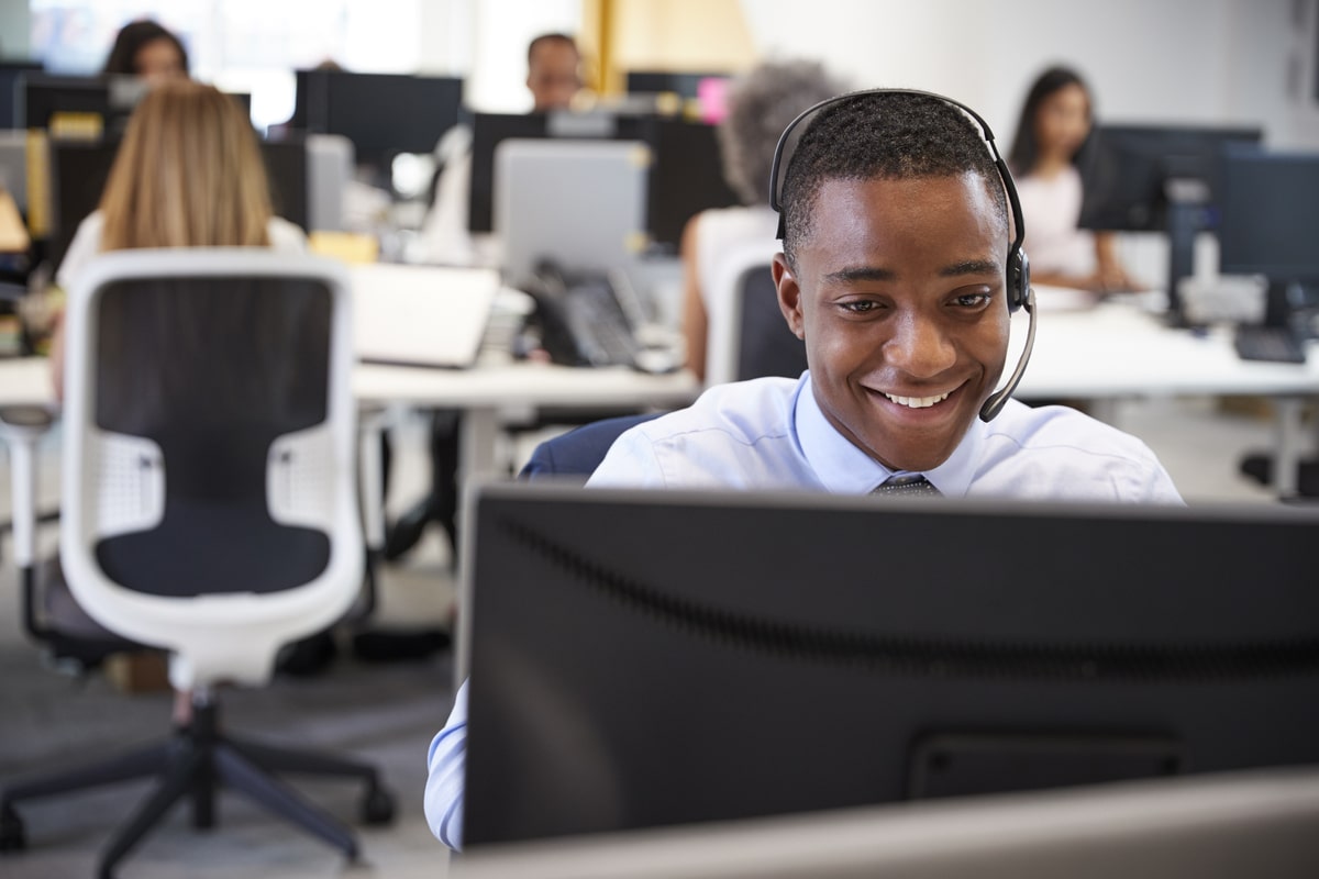 young-man-working-at-computer-with-headset-in-busy-2023-11-27-05-11-31-utc-min